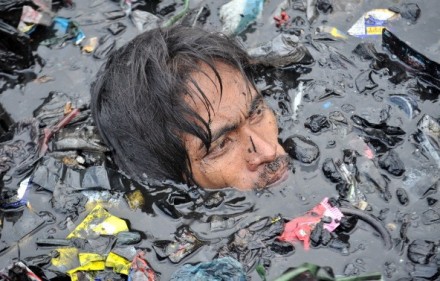 A resident swims among debris and rubbish looking for recyclab