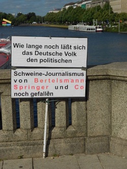 protest sign = how long will the German people put up with the pork-journalism of Bertelsmann, Springer and Co