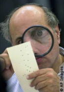 An election worker closely examines a Florida punch card ballot from the 2000 US Presidential election for signs of a hanging chad.